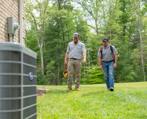 HVAC technicians walking up to an outdoor unit with tools